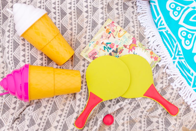 Bright and playful summer flat lay with beach essentials and quirky tumblers on a patterned cloth.
