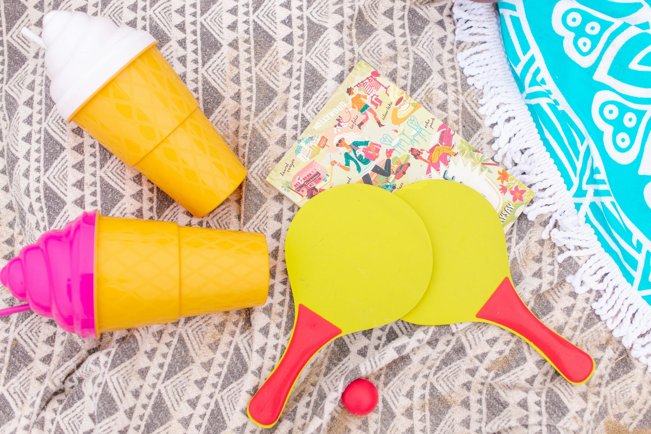 Bright and playful summer flat lay with beach essentials and quirky tumblers on a patterned cloth.